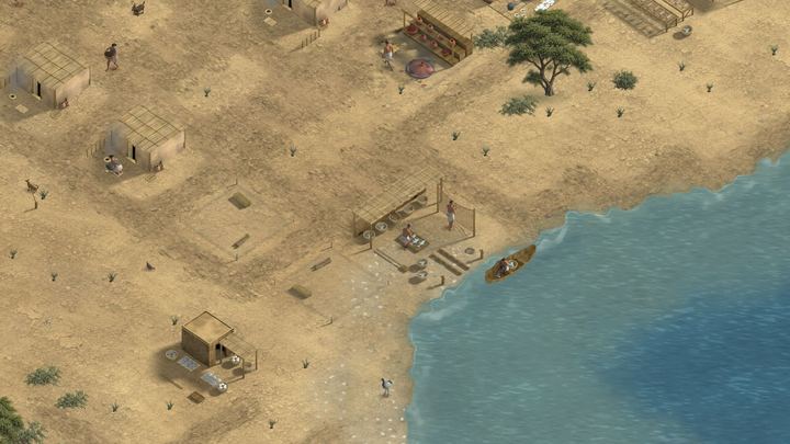 A sandy shore with a boat on the water, huts and work sheds.